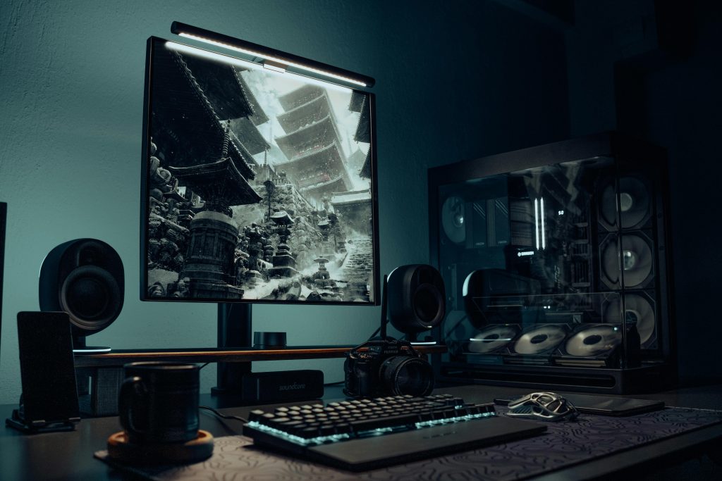 A sleek gaming desk setup with illuminated PC, monitor displaying Asian temple image, and accessories.