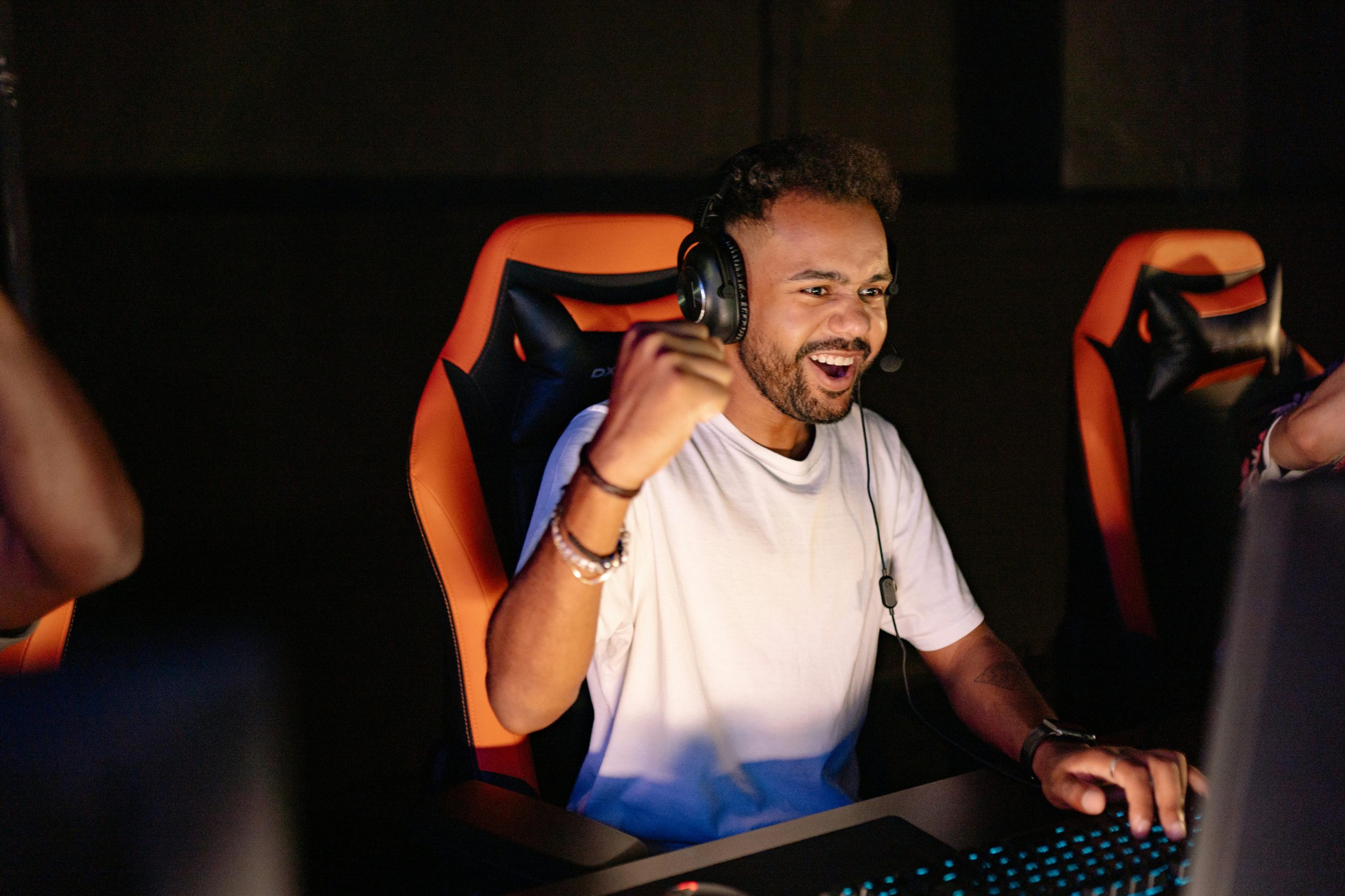 A man celebrating a win in a gaming chair, wearing headphones and using a PC.